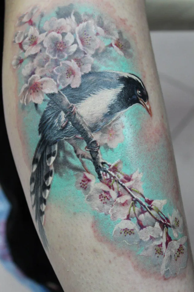 Тату сорока на ветке яблони в цвету на голени