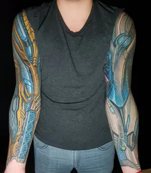 Татуировки в стиле киберпанк на обеих руках, сочетающие золотистые и синие оттенки, с изображением сложных технологических элементов и механических конструкций, создающих эффект высокотехнологичной обработки.